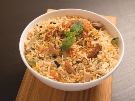 Λευκό μπωλ με ρύζι με κοτόπουλο, λαχανικά και Σπιρουλίνα flakes πάνω σε ξύλινο πάγκο