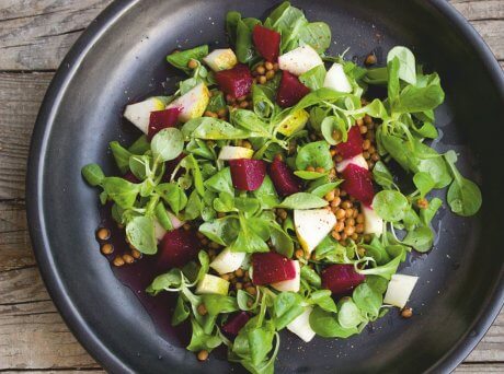 Μαύρο πιάτο σε ξύλινο πάγκο που περιέχει βαλεριάνα, παντζάρια, φακή και Σπιρουλίνα flakes