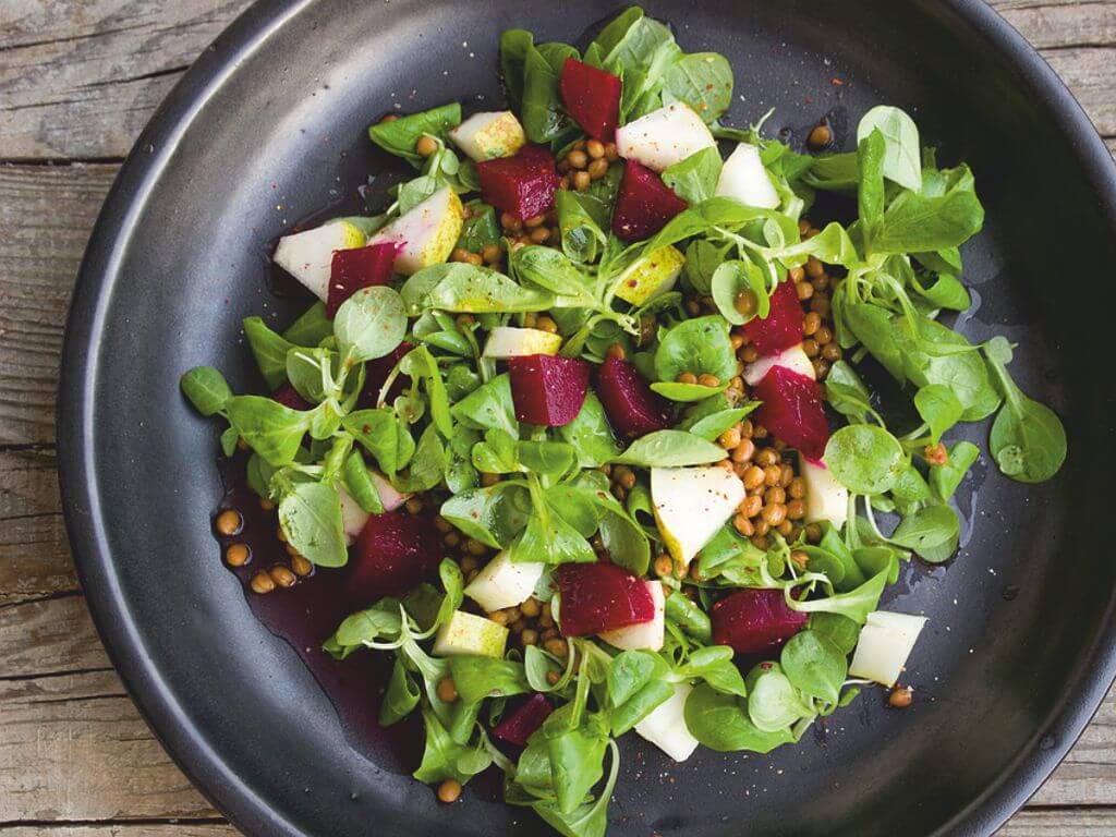 Μαύρο πιάτο σε ξύλινο πάγκο που περιέχει βαλεριάνα, παντζάρια, φακή και Σπιρουλίνα flakes