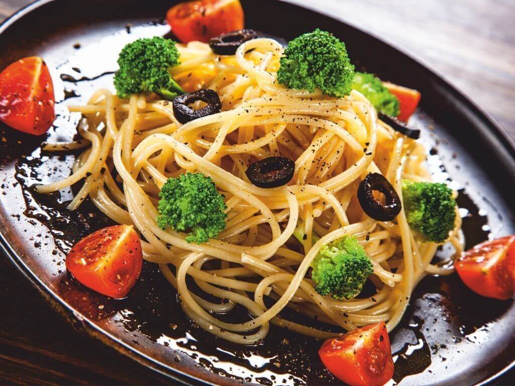 Μακαρόνια με μπρόκολο, ντοματίνια, ροδέλες ελιάς και Σπιρουλίνα flakes σερβιρισμένα σε καφέ πιάτο