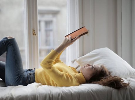Γυναίκα που διαβάζει ένα βιβλίο ξαπλωμένη στο κρεβάτι δίπλα σε ένα παράθυρο