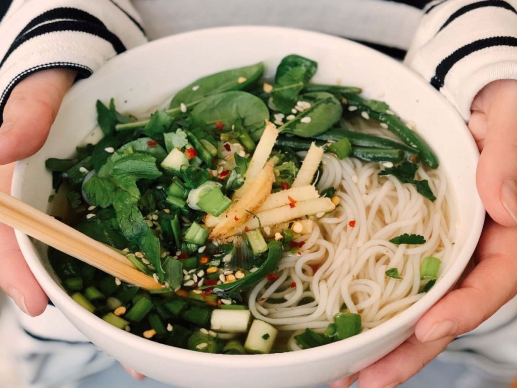 Γυναίκα με ριγέ μπλούζα που κρατάει ένα μπολ με λαχανικά και ζυμαρικά