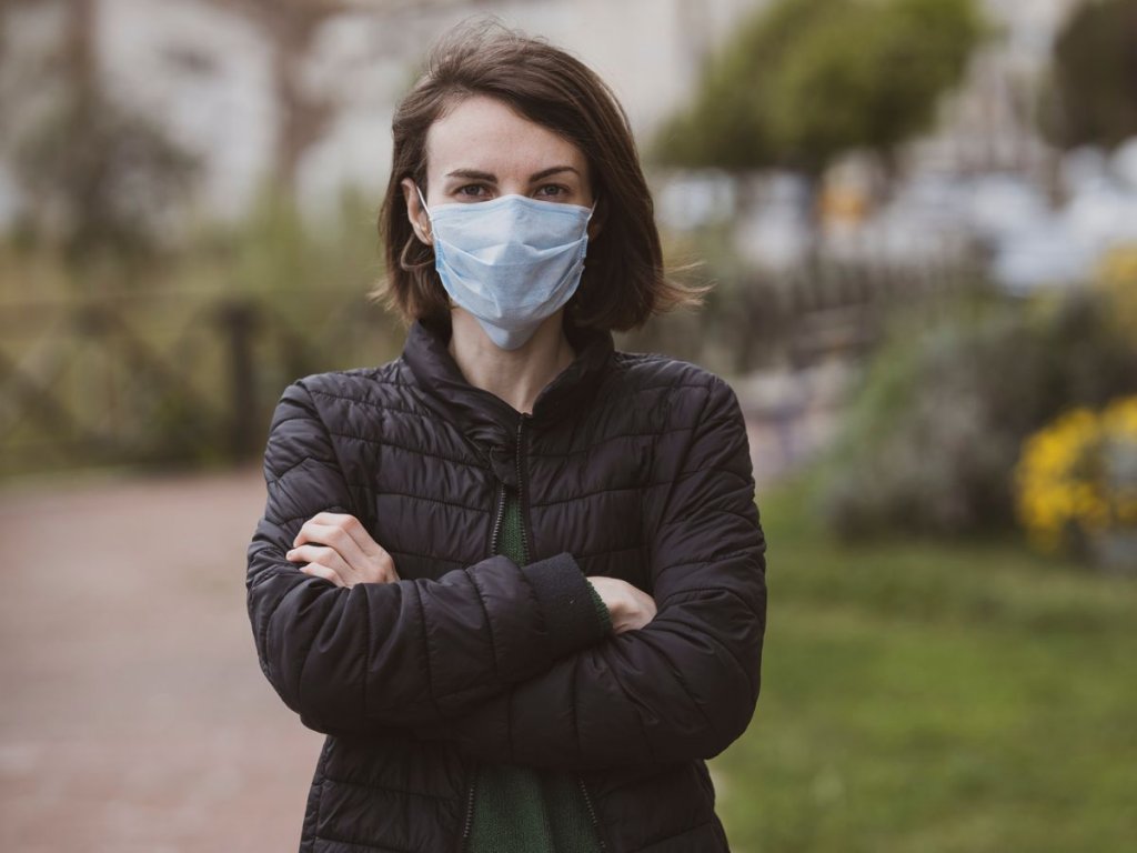 Γυναίκα με καστανά μαλλιά φοράει χειρουργική μάσκα σε εξωτερικό χώρο