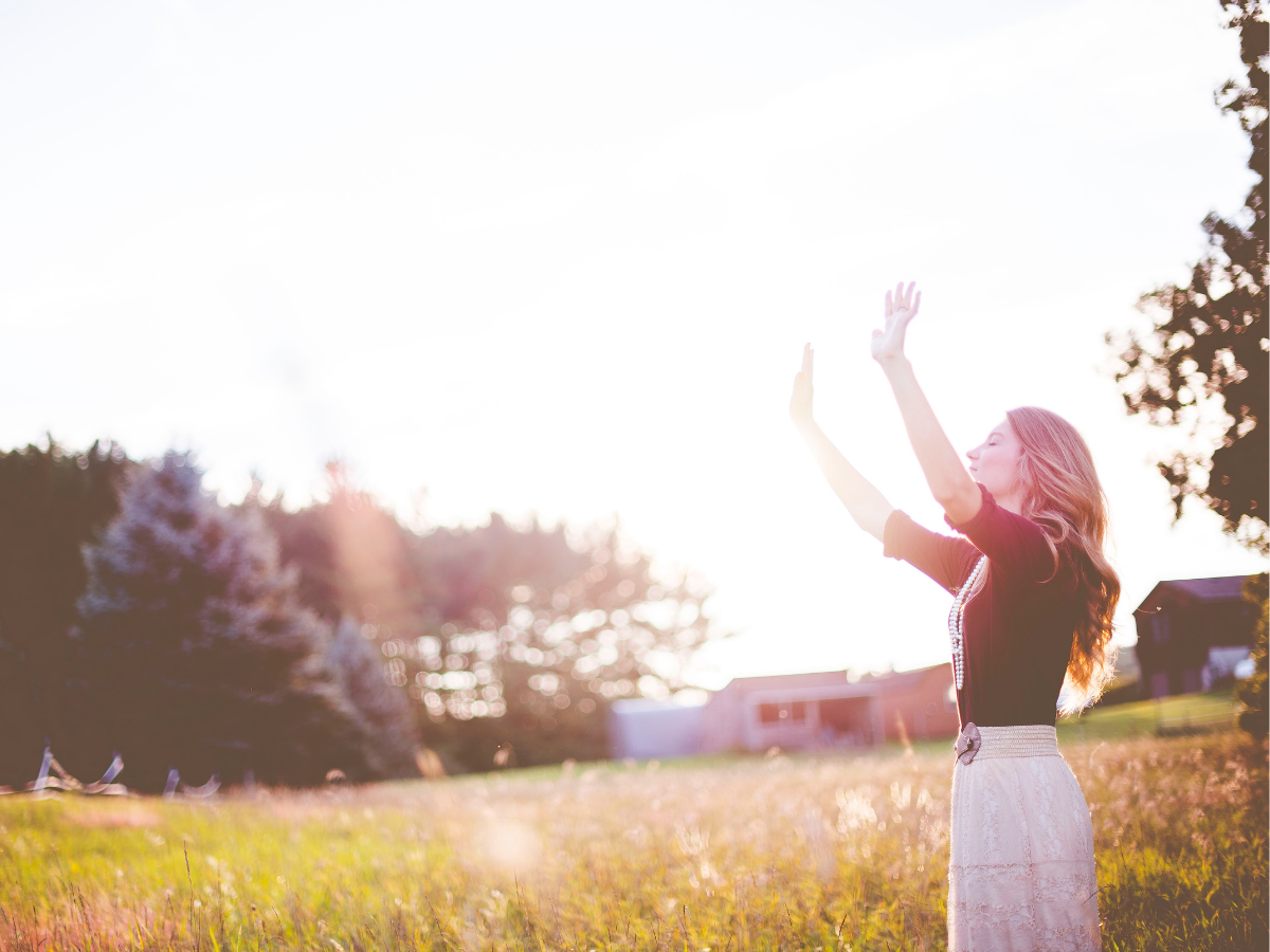 Νεαρή γυναίκα με τα χέρια ψηλά στην εξοχή