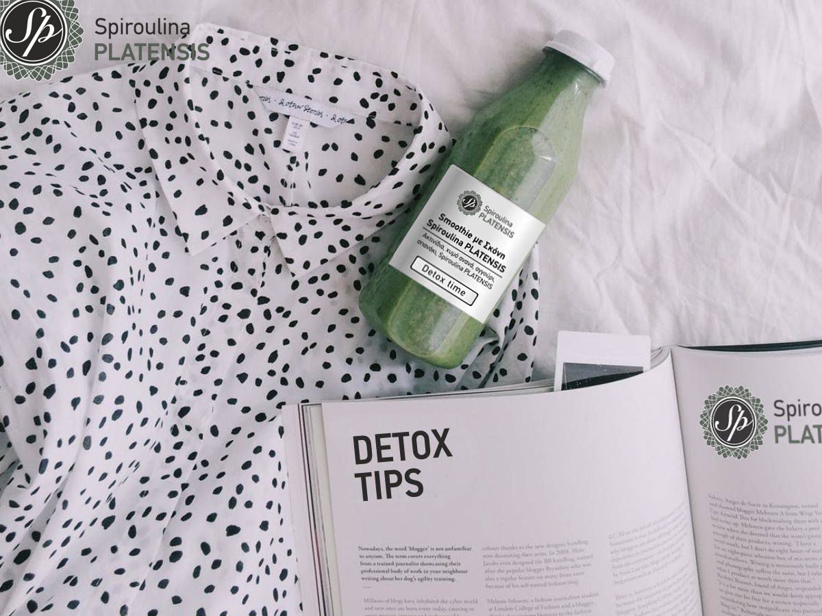 Ένα μπουκάλι με πράσινο smoothie πάνω σε κρεβάτι, δίπλα σε ένα πουκάμισο πουά και ένα ανοιχτό περιοδικό