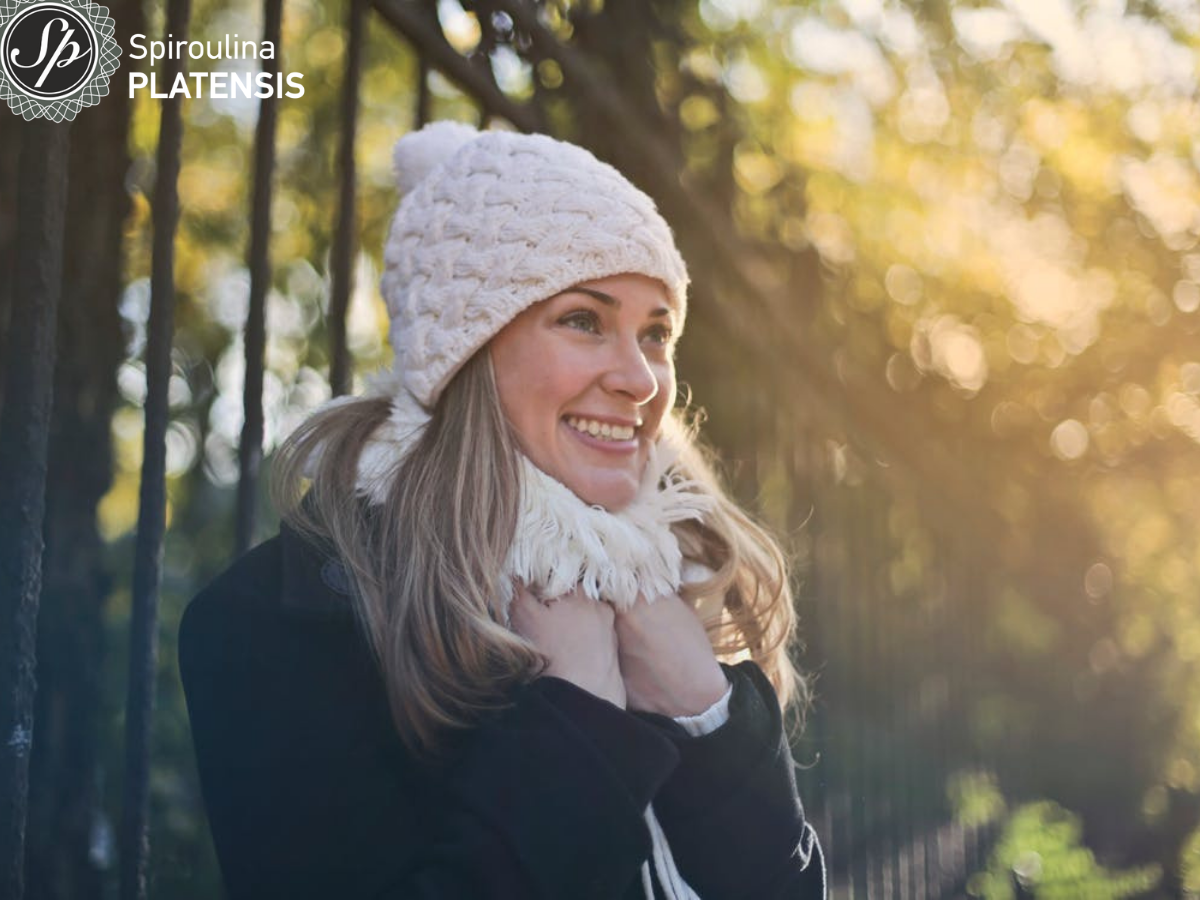 Νεαρή γυναίκα με σκουφί και κασκόλ σε δάσος χαμογελάει