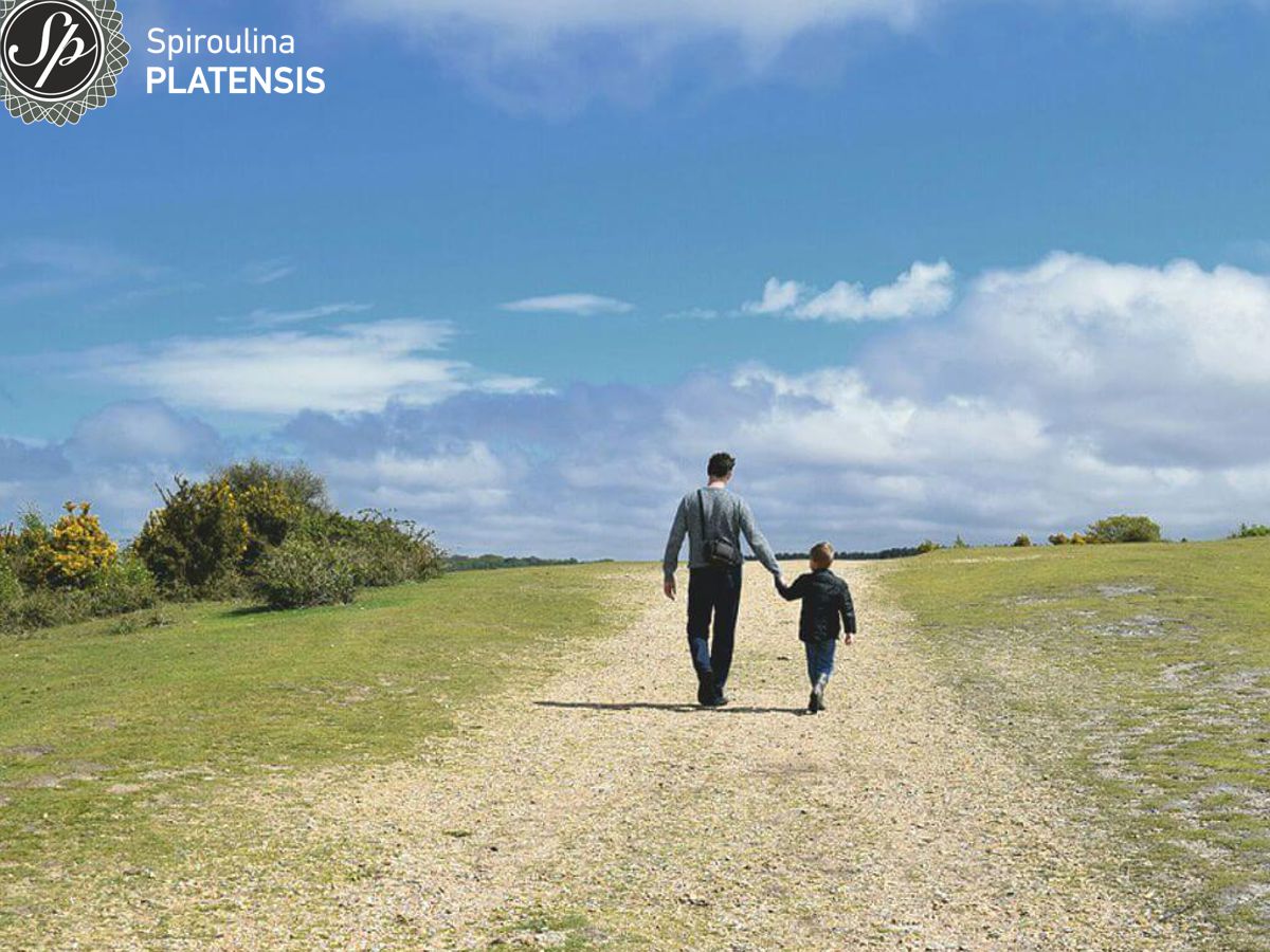 Πατέρας με γιο πιασμένοι χέρι χέρι περπατούν σε ένα όμορφο τοπίο με πράσινο και γαλάζιο ουρανό