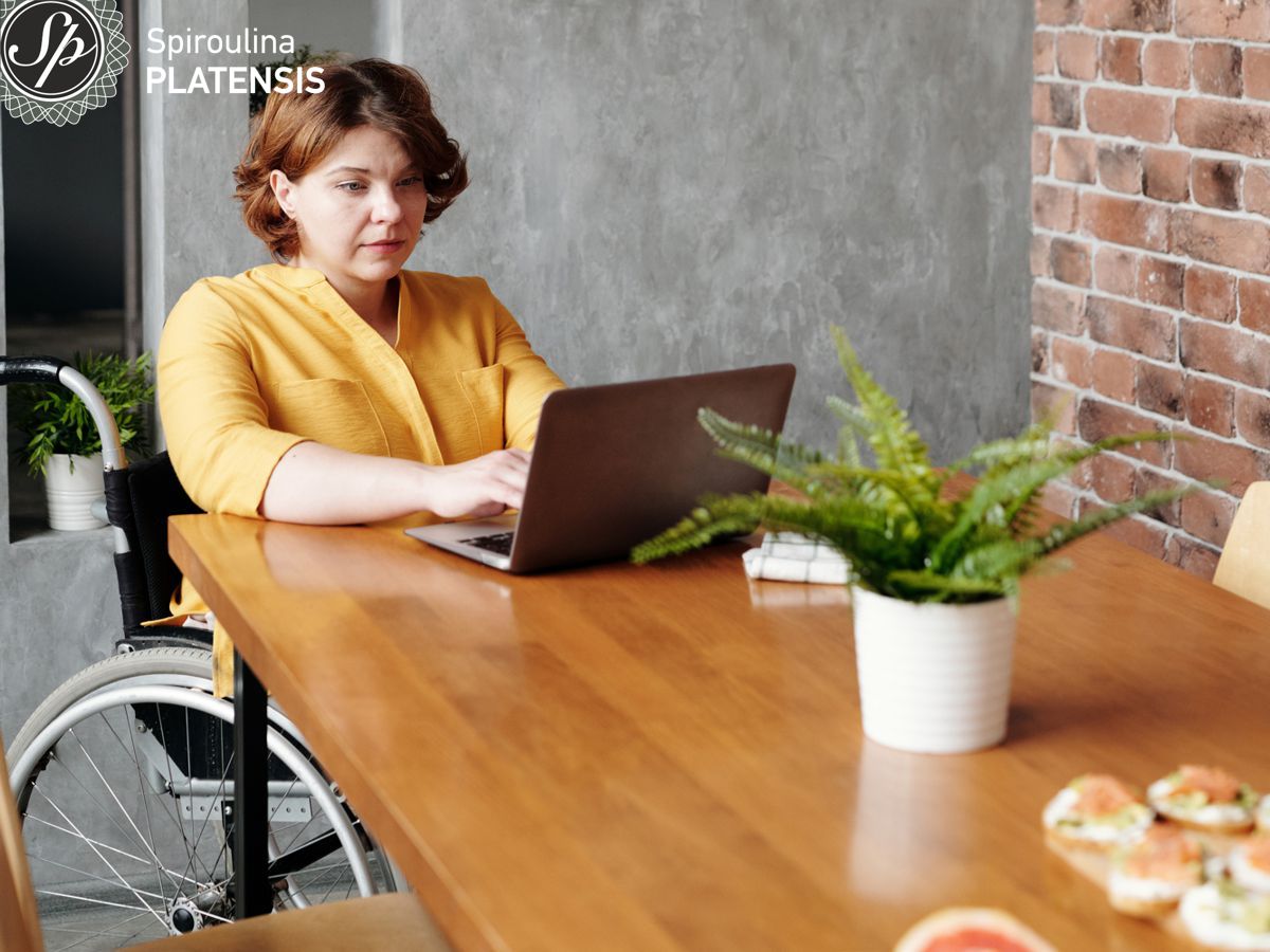 Γυναίκα σε αναπηρικό αμαξίδιο που δουλεύει σε υπολογιστή από το σπίτι της
