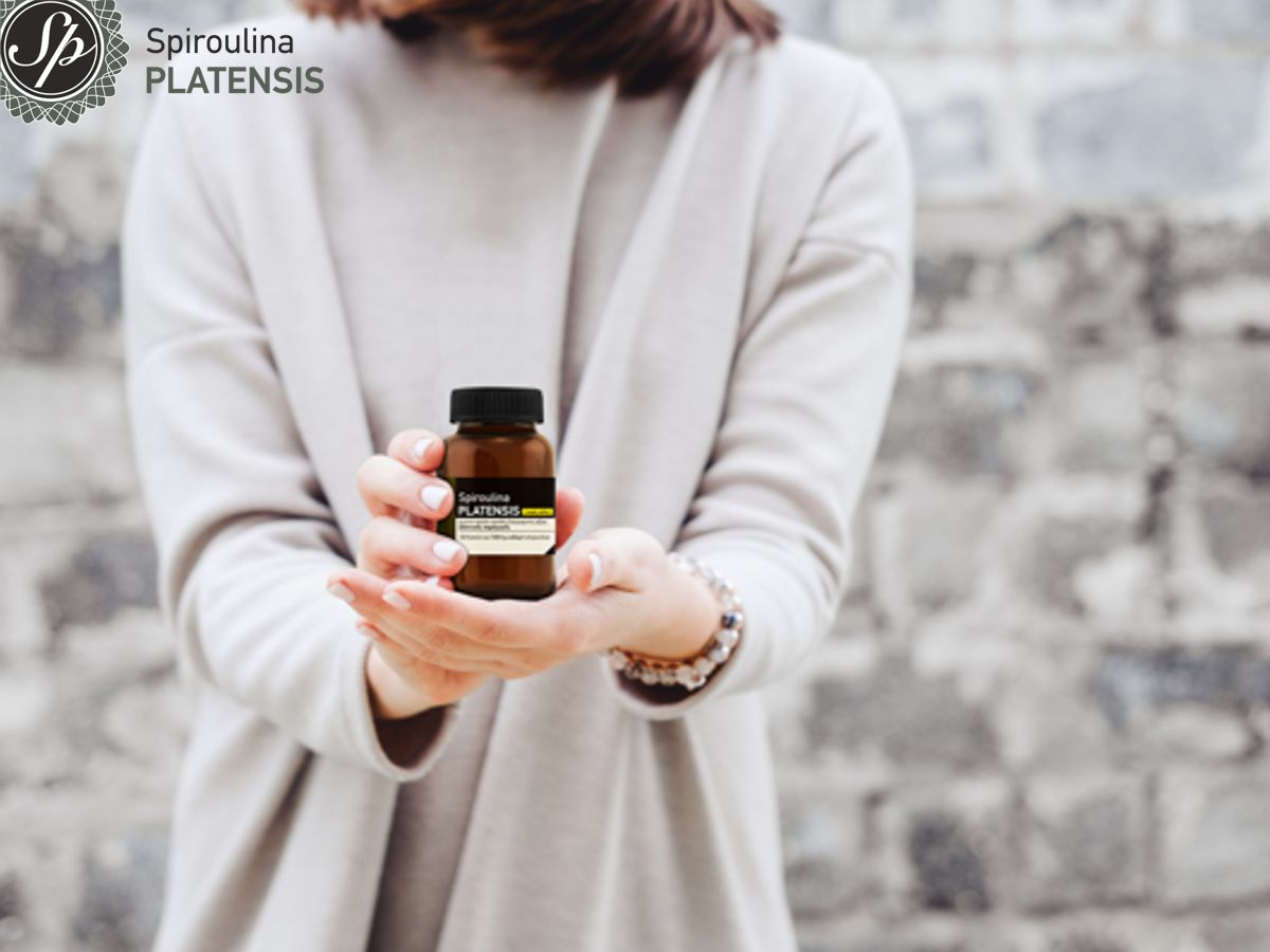 Γυναίκα με γκρι ρούχα κρατάει στα χέρια της ένα μπουκάλι Spiroulina PLATENSIS