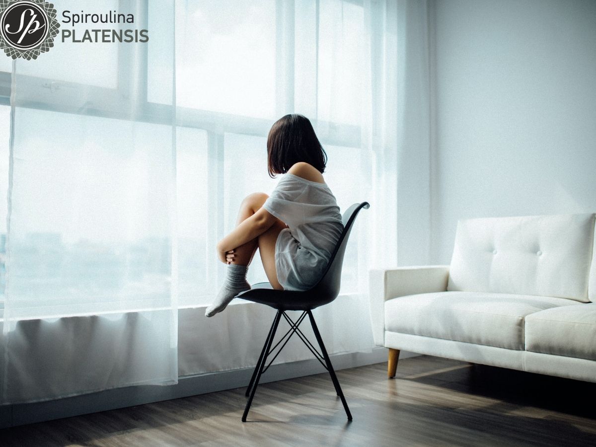 Κοπέλα που κάθεται πίσω από ένα παράθυρο με λευκή κουρτίνα