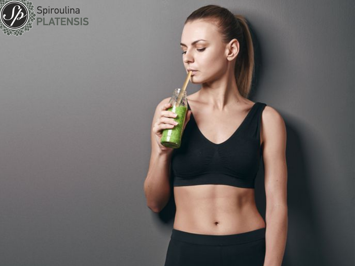 κοπέλα με αθήτικό ντύσιμο πίνει πράσιμο smoothie με spiroulina platensis και bamboo καλαμάκι
