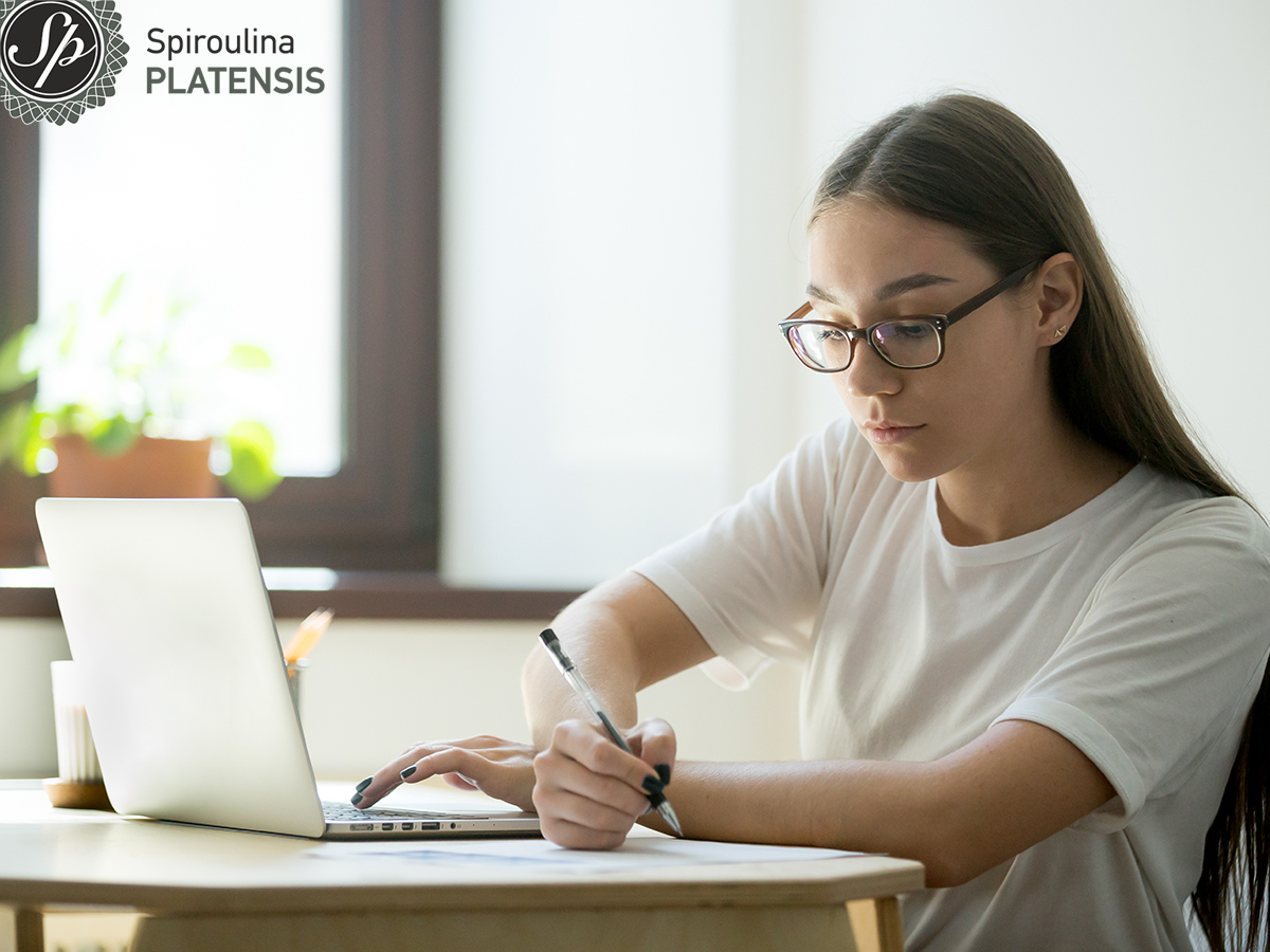 Νεαρή μαθήτρια που διαβάζει στον υπολογιστή και κρατάει σημειώσεις