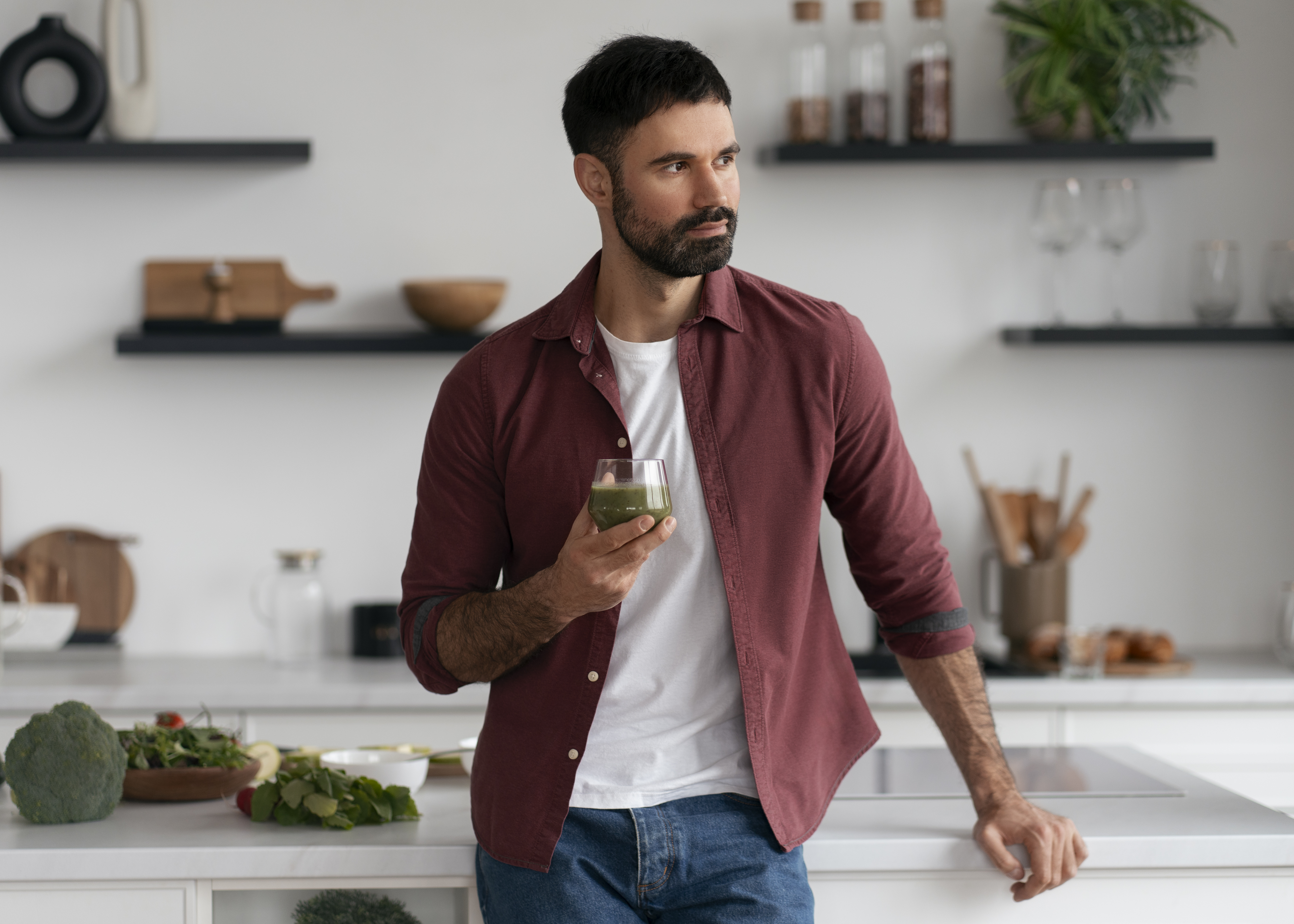 Άνδρας στην κουζίνα κρατά ποτήρι με πράσινο ρόφημα (smoothie) και εμφανίζεται το λογότυπο Spiroulina PLATENSIS, εικόνα για άρθρο «Τι συμβαίνει στο σώμα σου όταν παίρνεις Spiroulina PLATENSIS».