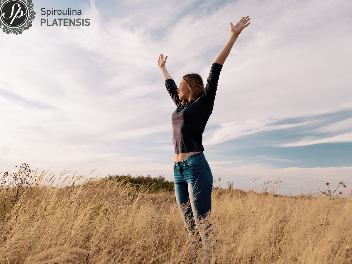 Νεαρή γυναίκα σε αγρό με ανοιχτά τα χέρια που νιώθει ευεξία