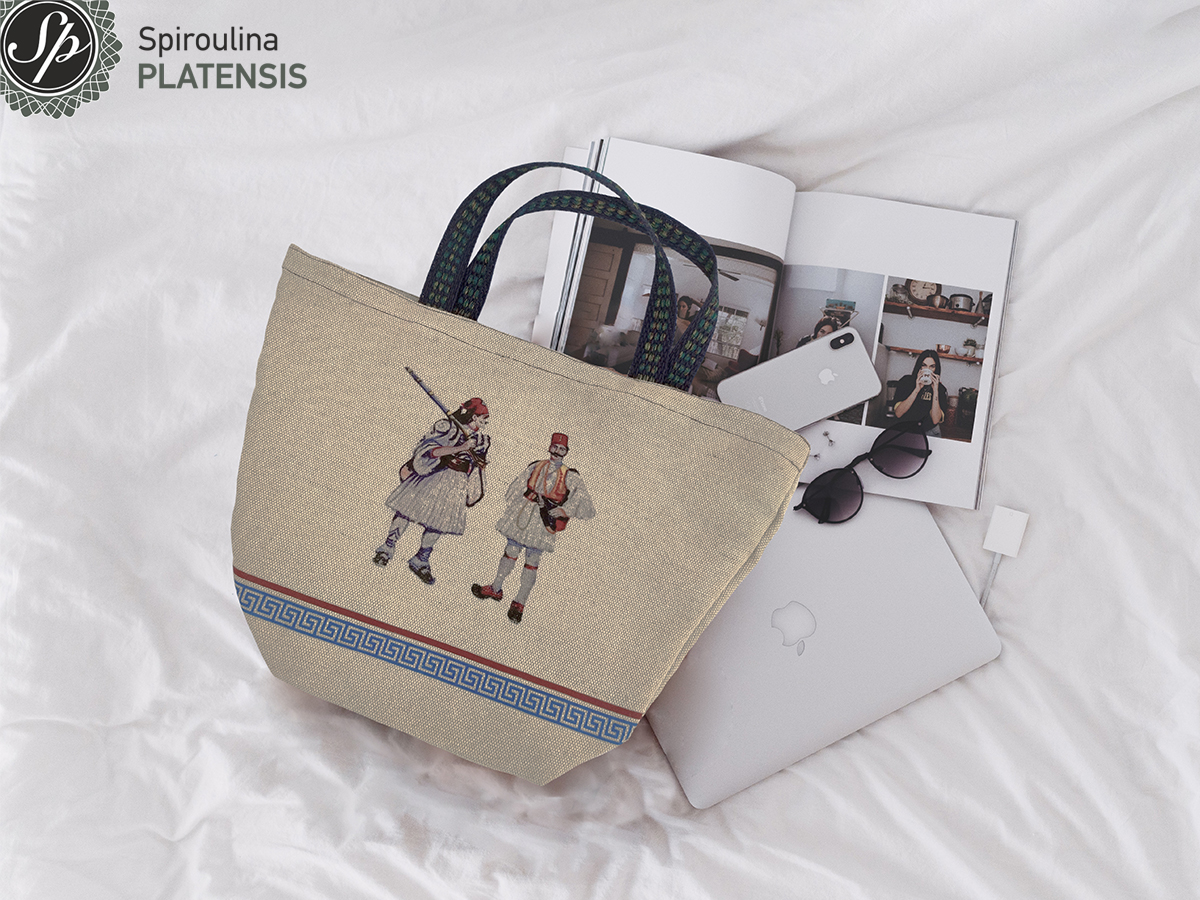 Evzones bag πάνω σε κρεβάτι με λευκό σεντόνι ένα iphone & macbook δίπλα