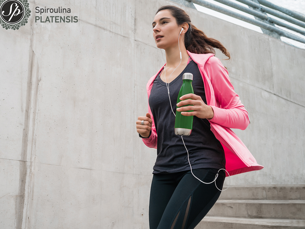 Γυναίκα που κάνει το πρωινό της τρέξιμο και κρατάει ένα μπουκάλι με smoothie με Spiroulina PLATENSIS