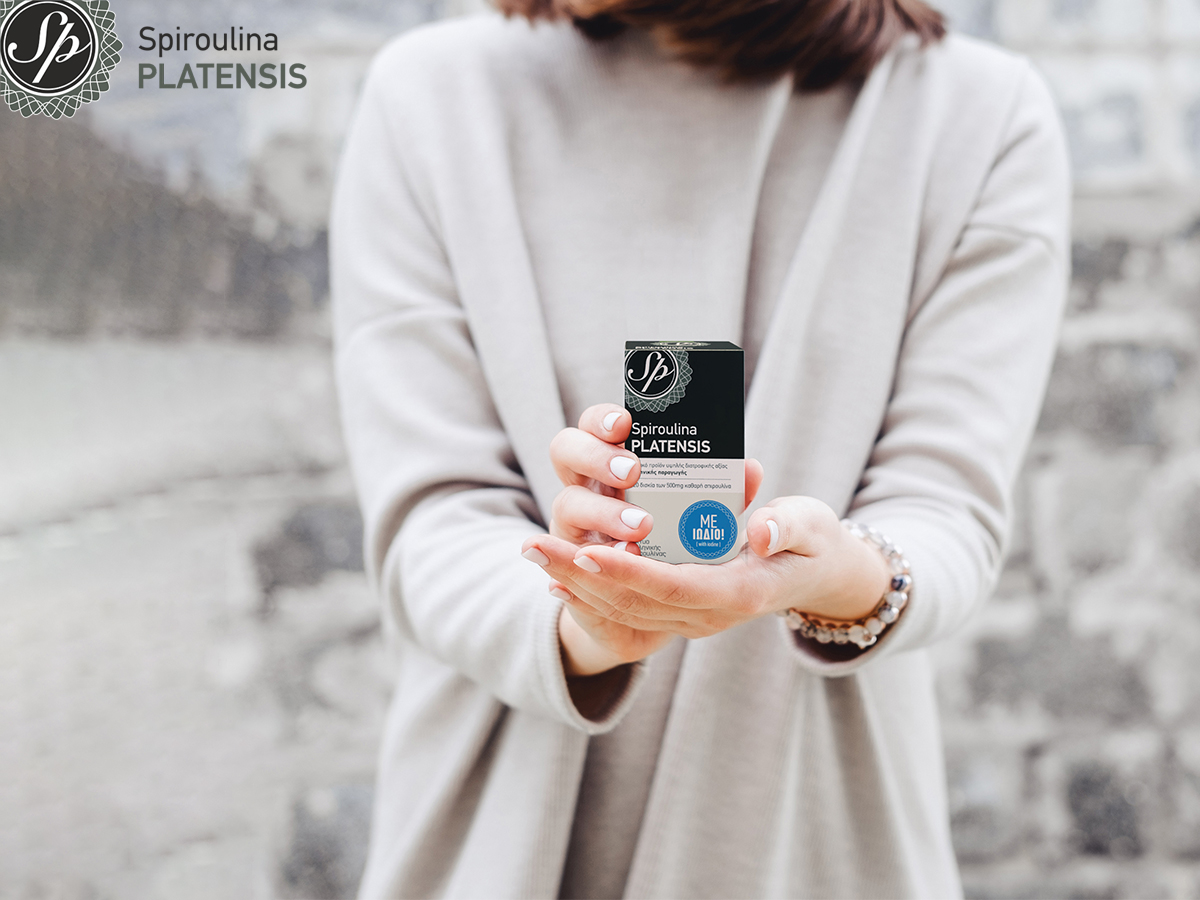 Γυναίκα με γκρι πουλόβερ κρατάει μία συσκευασία Spiroulina PLATENSIS Με Ιώδιο