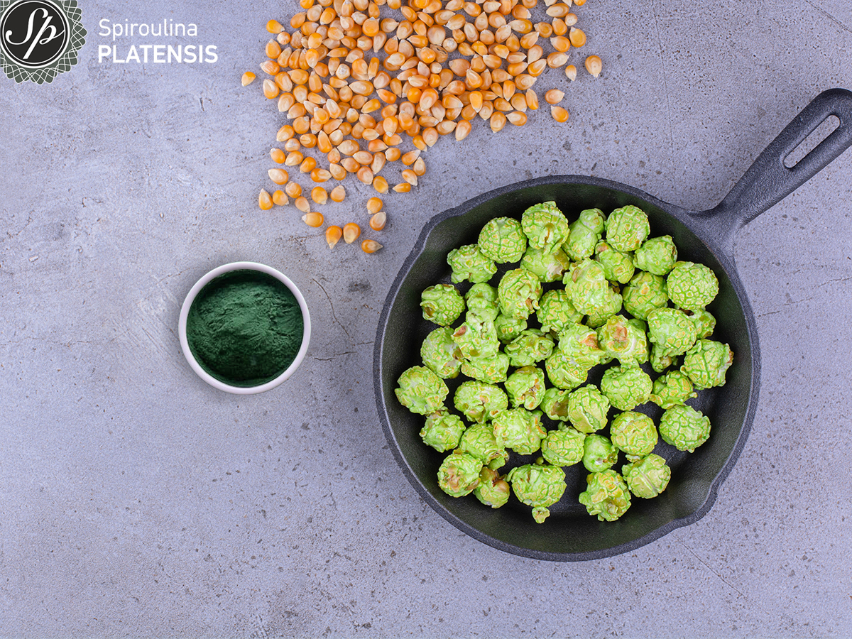 Τηγάνι με πράσινα ποπ-κορν σε γκρι πάγκο με καλαμπόκι κι ένα μπολάκι με σκόνη Spiroulina PLATENSIS