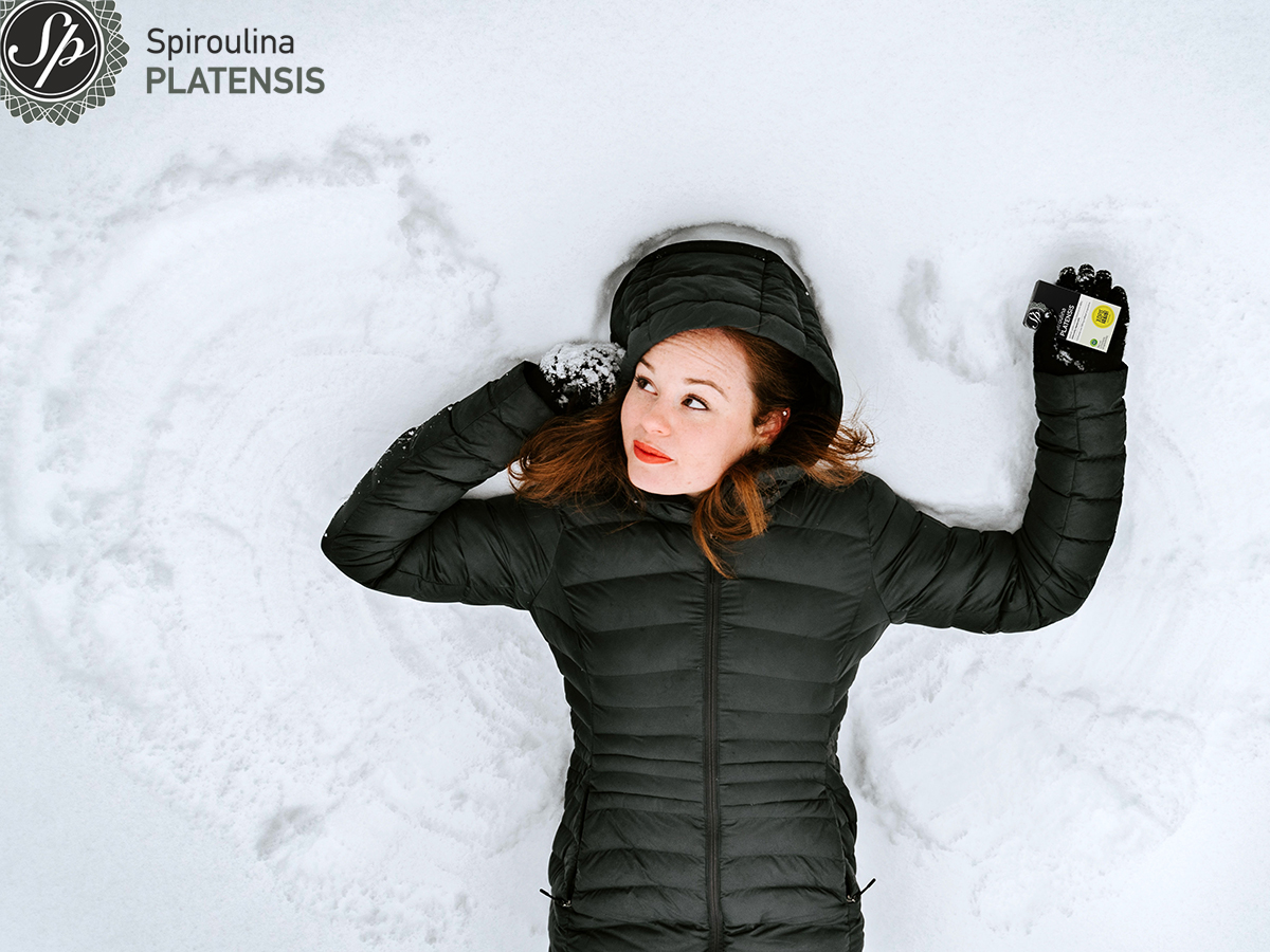 Νεαρή κοπέλα που κρατά spiroulina PLATENSIS στο χέρι είναι ξαπλωμένη στα χιόνια