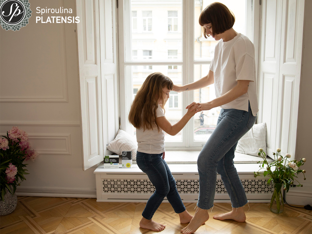 Μητέρα και κόρη με λευκό μπλουζάκι και τζιν χορεύουν μπροστά από ένα παράθυρο