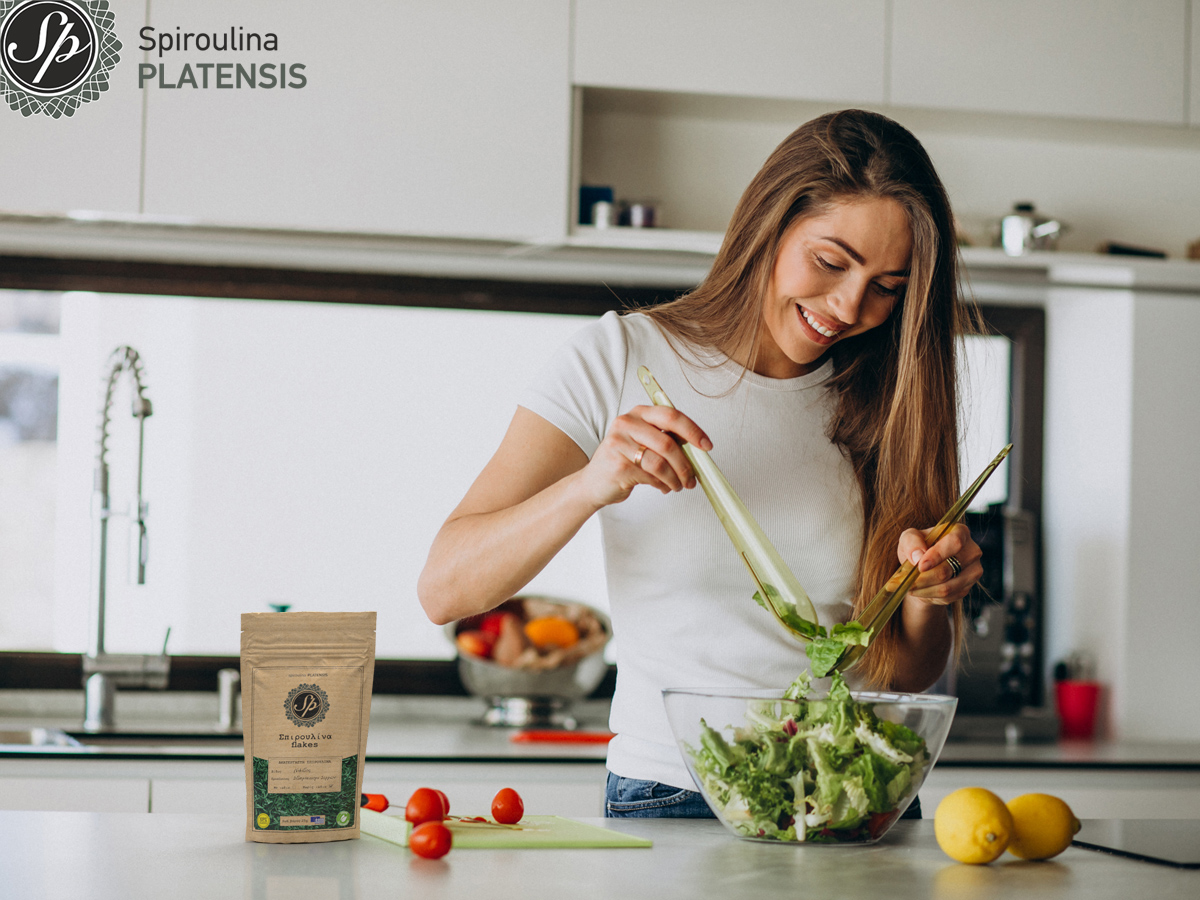 Νεαρή γυναίκα που φτιάχνει σαλάτα με σπιρουλίνα flakes