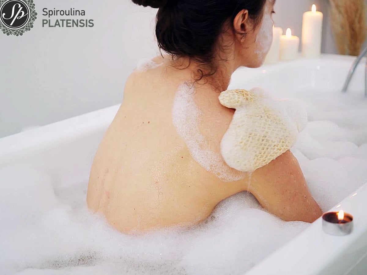 Νεαρή γυναίκα στο μπάνιο που κάνει απολέπιση με το γάντι από ίνες γιούτας και κάνναβης