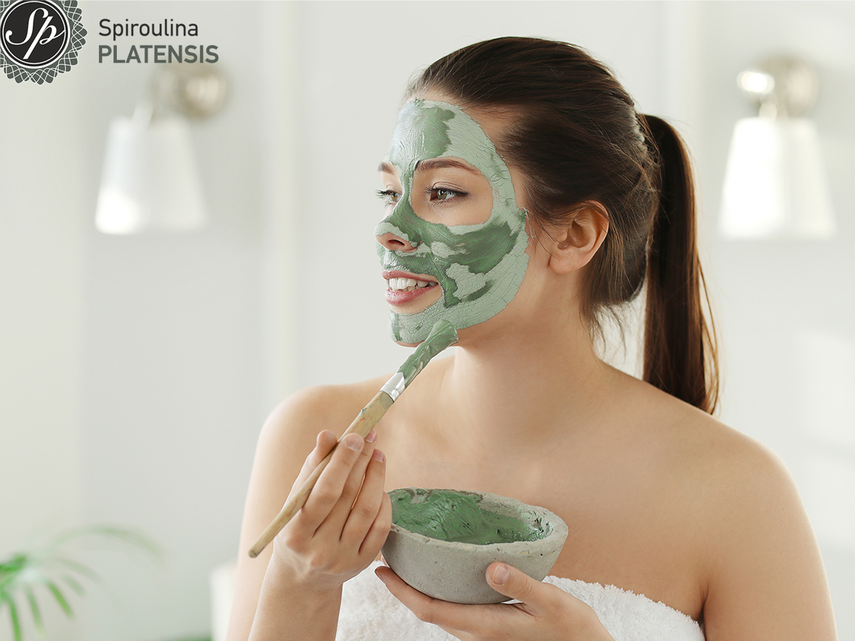 Νεαρή μελαχρινή γυναίκα που εφαρμόζει πράσινη μάσκα ομορφιάς με spiroulina PLATENSIS στο πρόσωπό της