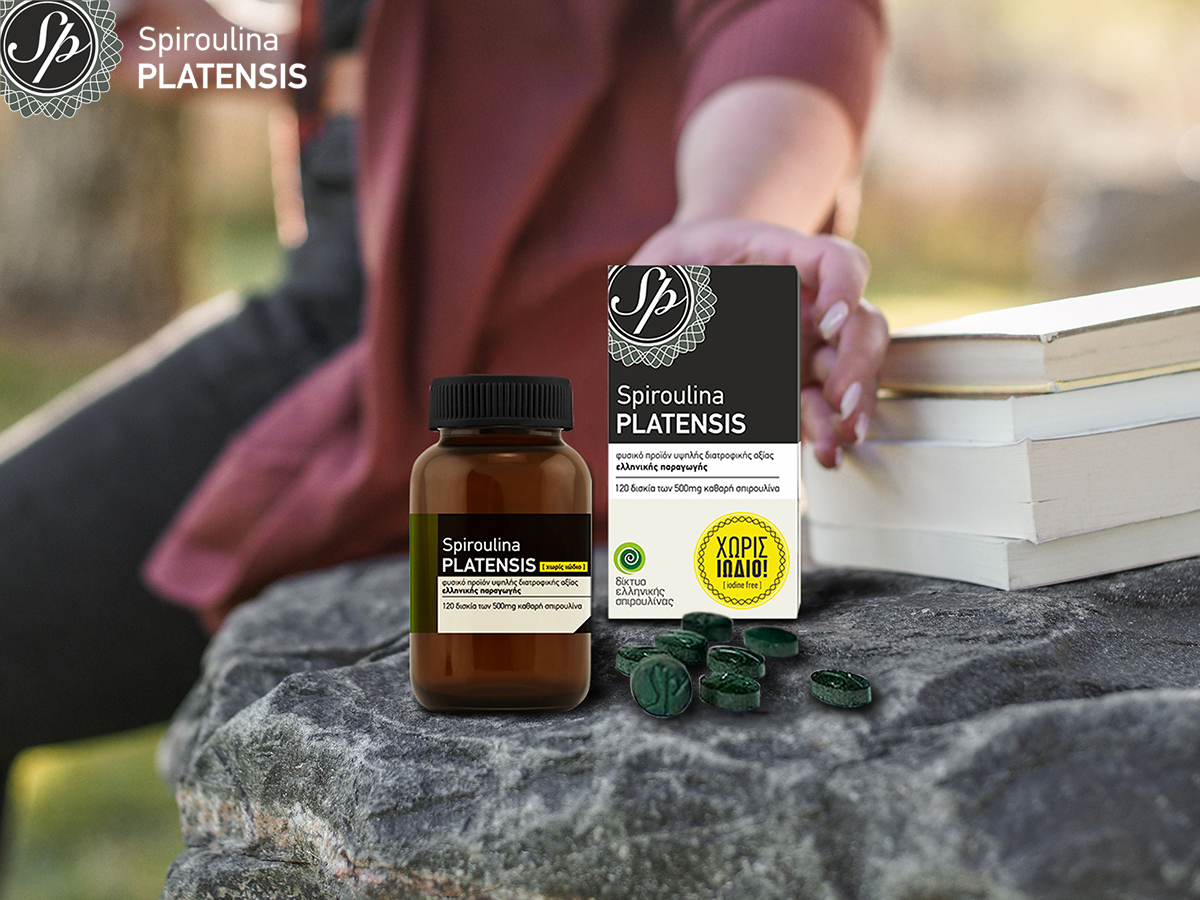 Μία γυναίκα σε εξωτερικό χώρο πιάνει μία συσκευασία spiroulina PLATENSIS ταμπλέτες χωρίς ιώδιο