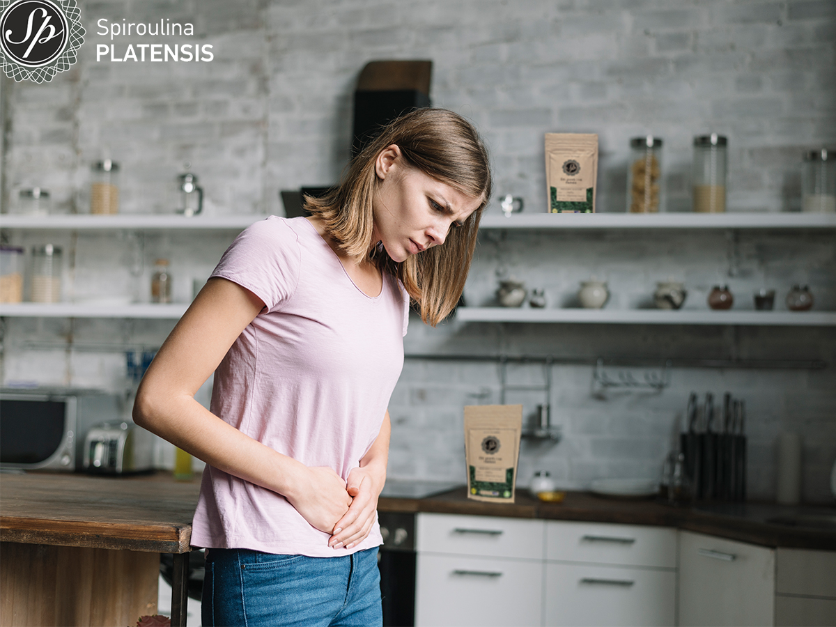 Νεαρή γυναίκα που φοράει ρόζ κοντομάνικο μπλουζάκι και υζην πιάνει την κοιλιά της χαμηλά σε εσωτερικό χώρο