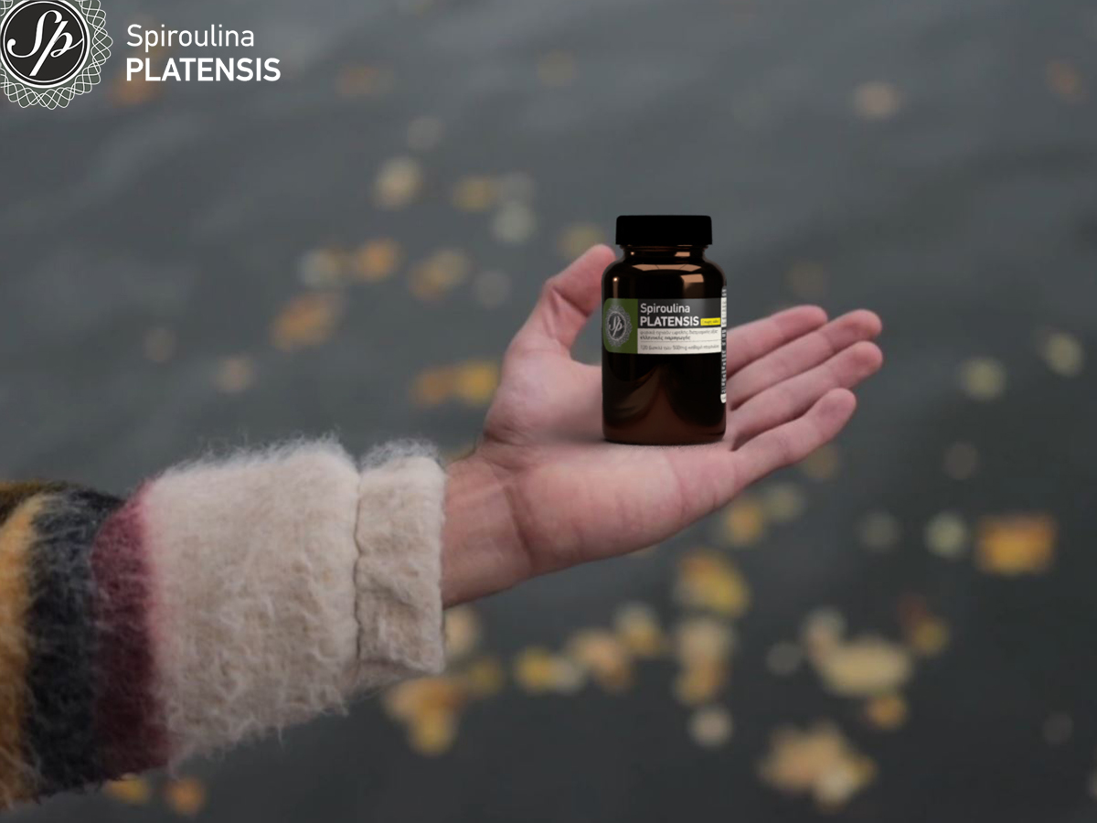 Χέρι πάνω από μία λίμνη που κρατάει ένα μπουκάλι spiroulina PLATENSIS ταμπλέτες χωρίς ιώδιο