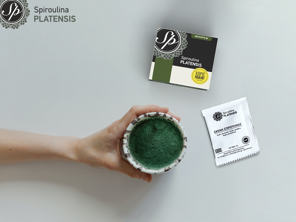 Χέρι που κρατάει ένα ποτήρι με ρόφημα με σκόνη Spiroulina PLATENSIS