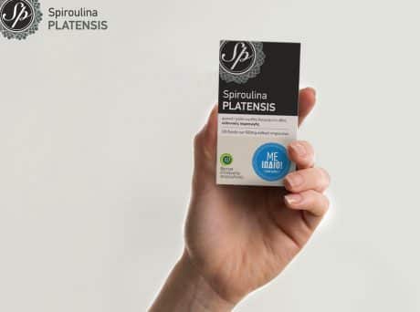 Χέρι κρατά συσκευασία Spiroulina PLATENSIS Με Ιώδιο σε ουδέτερο φόντο