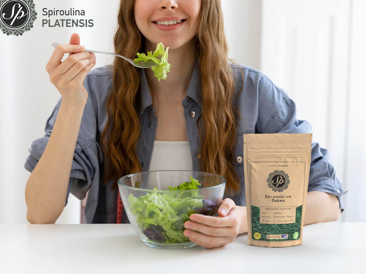 Νεαρή γυναίκα με τζιν πουκάμισο τρώσει σαλάτα με Σπιρουλίνα flakes