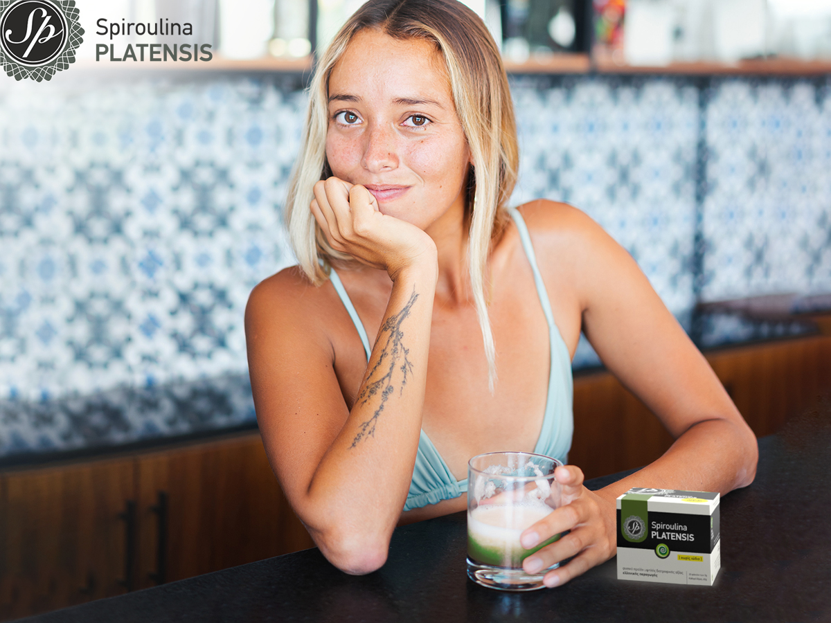 Νεαρή ξανθιά γυναίκα που κρατάει ένα ποτήρι με smoothie δίπλα από μία συσκευασία με σκόνη