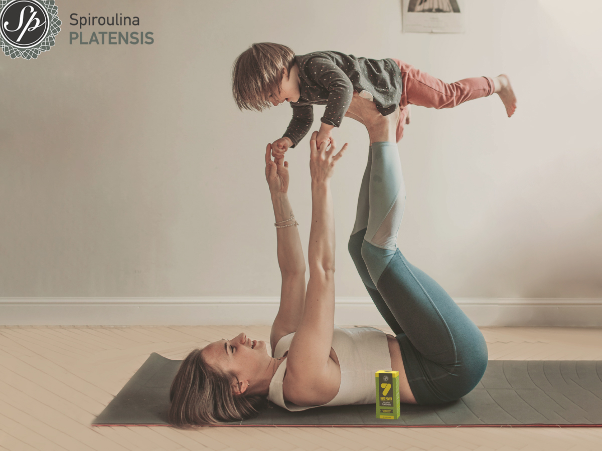 Μαμά η οποία κρατάει ψηλά στα πόδια της το παιδί της και δίπλα μία συσκευασία Spiroulina PLATENSIS
