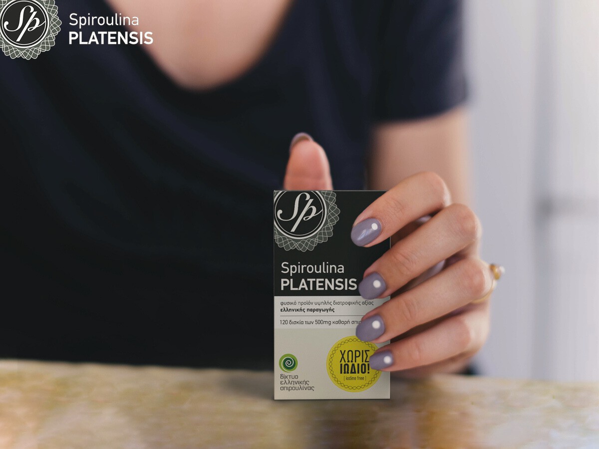 Μία γυναίκα με μαύρη μπλούζα που κρατάει μία συσκευασία Spiroulina PLATENSIS ταμπλέτες χωρίς ιώδιο