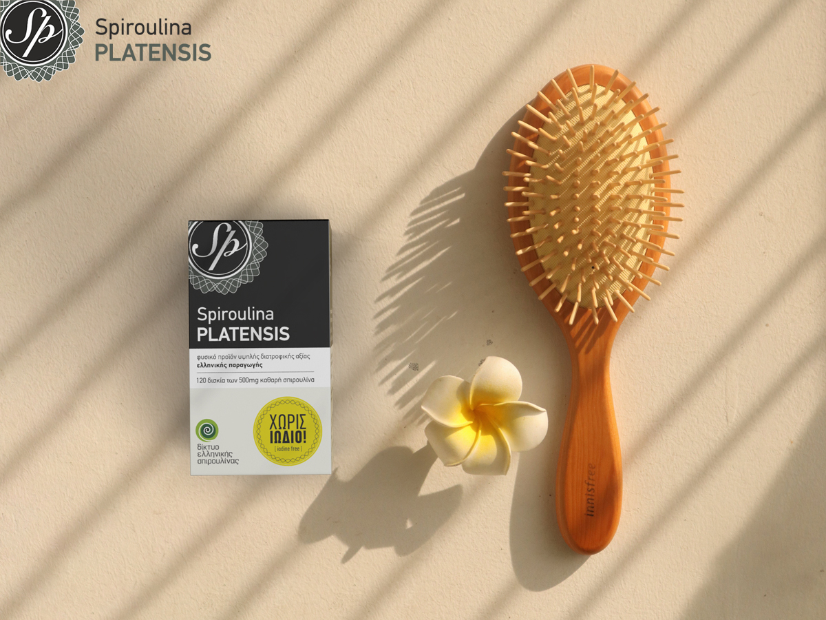 Μία συσκευασία spiroulina PLATENSIS ταμπλέτες χωρίς ιώδιο δίπλα σε μία βούρτσα μαλλιών σε μπεζ φόντο