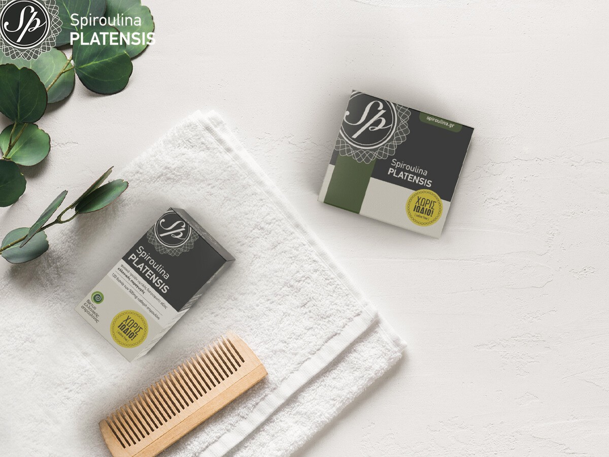 Δύο συσκευασίες Spiroulina PLATENSIS σε ταμπλέτες & σκόνη πάνω σε μία λευκή πετσέτα και δίπλα σε μία χτένα